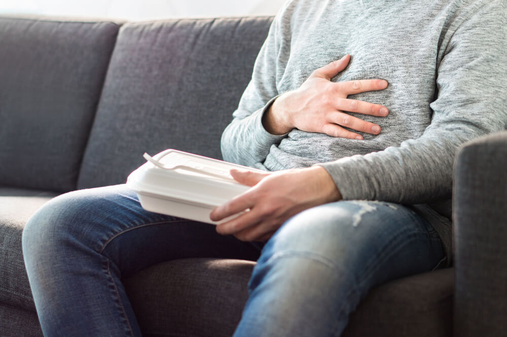 Man in Gray Sweater Holding His Stomach While Holding Take Out Food